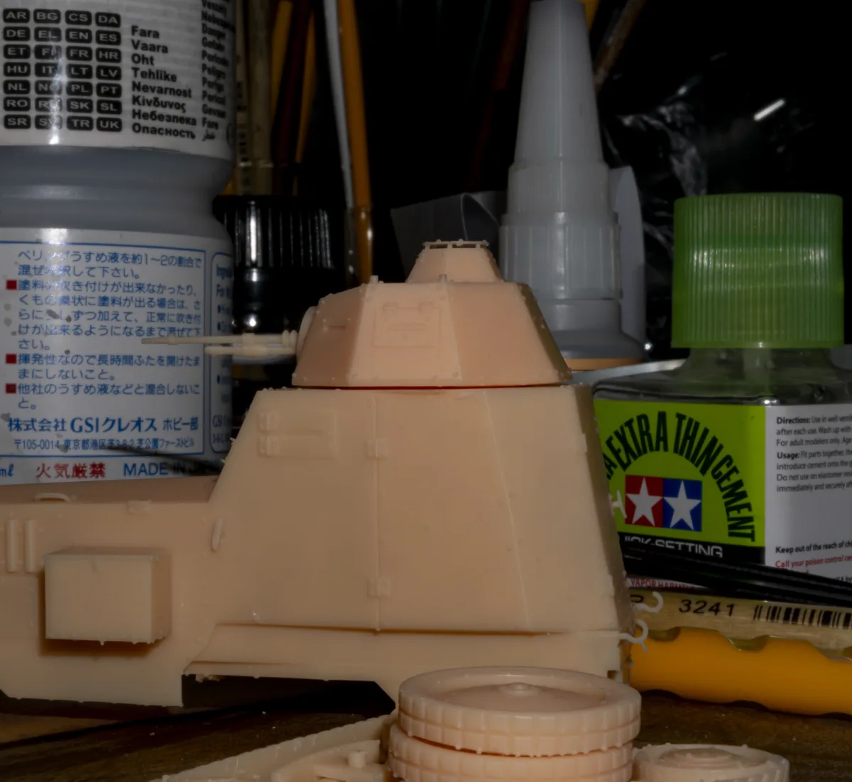 A close-up photo of an unpainted, beige plastic model kit part, likely a tank turret or hull section, sitting on a workbench…