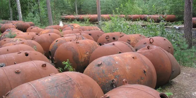 A field of rusted, abandoned, barrel-shaped metal containers lies scattered in a wooded area. Overlaid text reads 'i'm not a…
