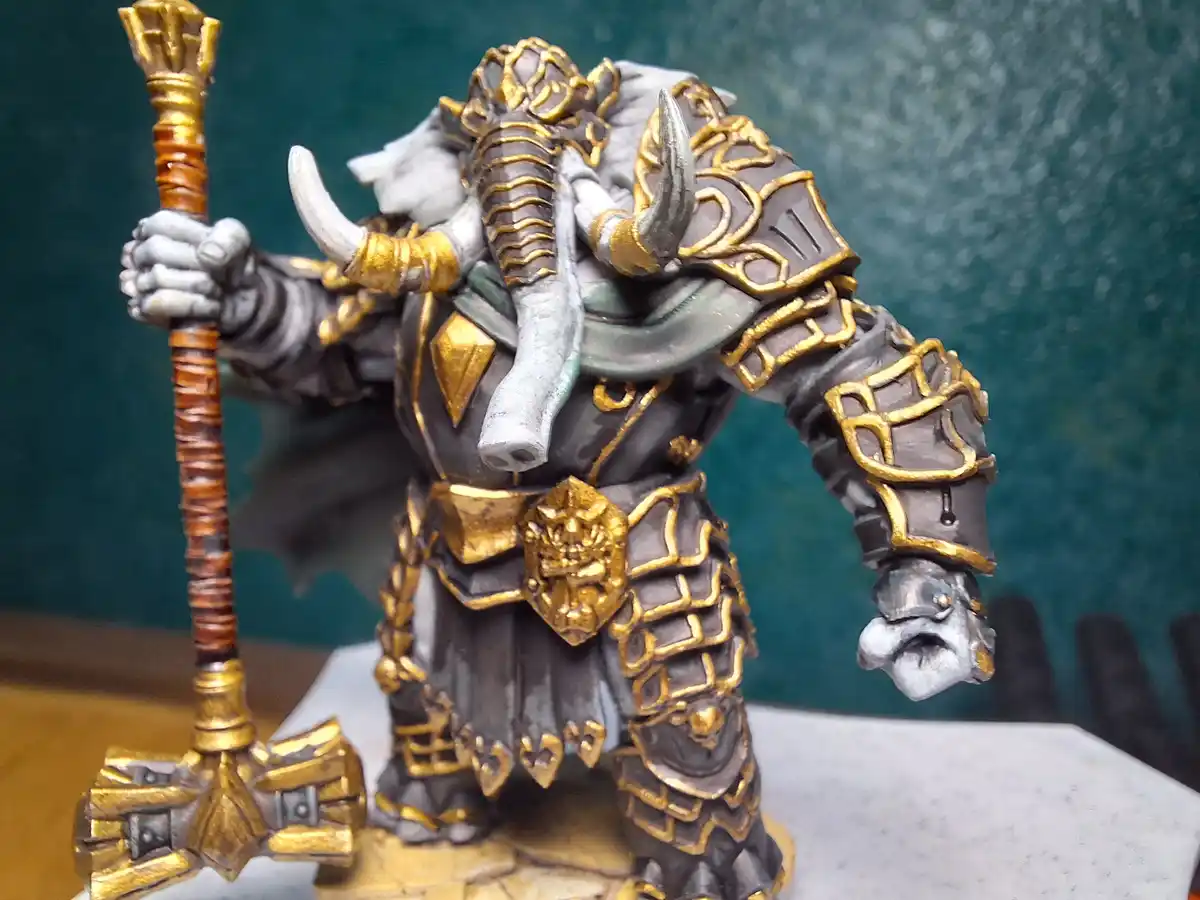 A heavily detailed miniature figurine of a fantasy warrior, likely a dwarf or orc, wearing ornate grey and gold armor with…