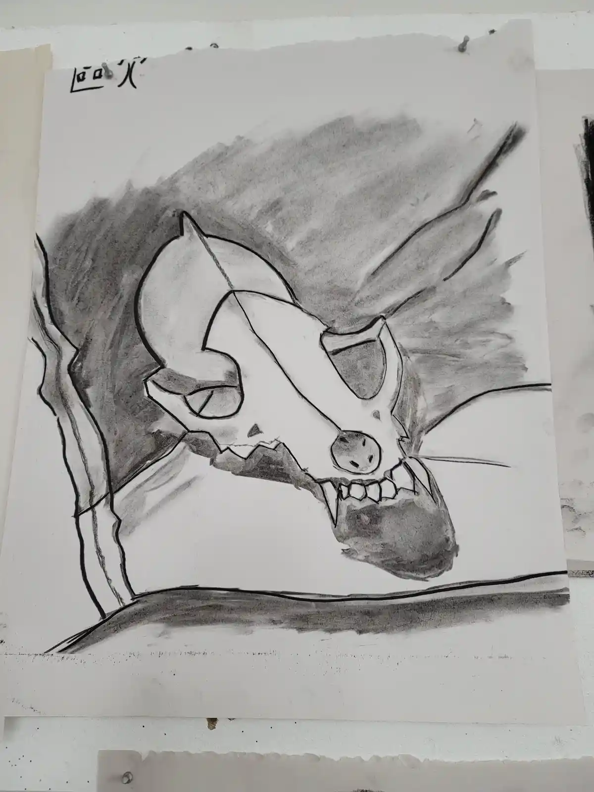 a charcoal and ink drawing on paper depicts a stylized animal skull with cat-like ears, whiskers, and a snarling expression…