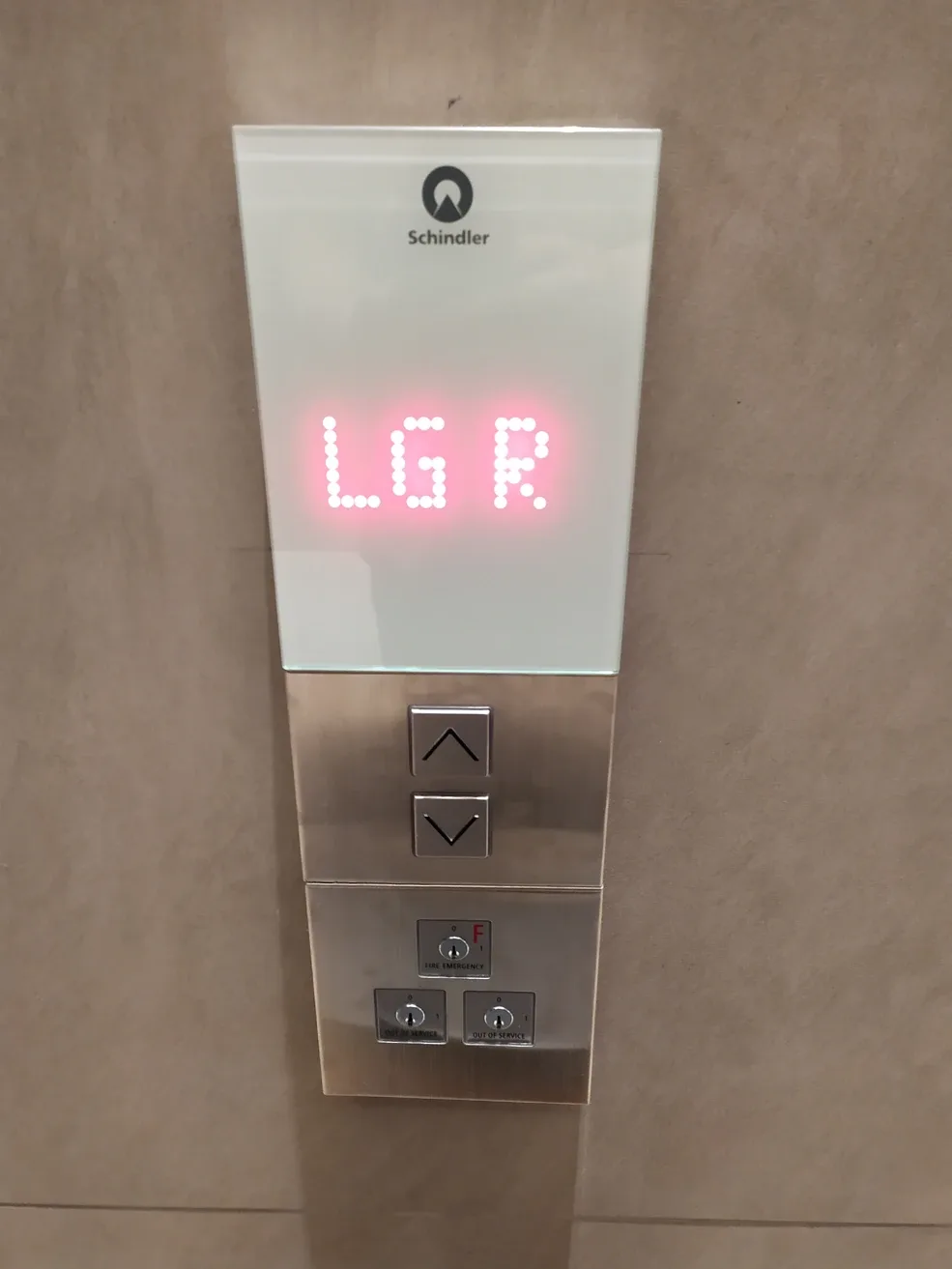A close-up photo of a Schindler elevator panel with a red LED display showing the letters 'LGR'. Below the display are…