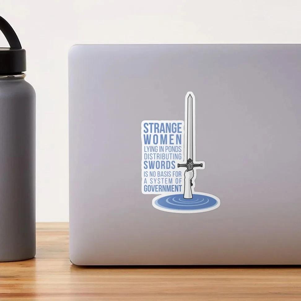 A sticker on a silver laptop lid shows a hand emerging from blue water holding a sword upright. The text reads 'STRANGE…