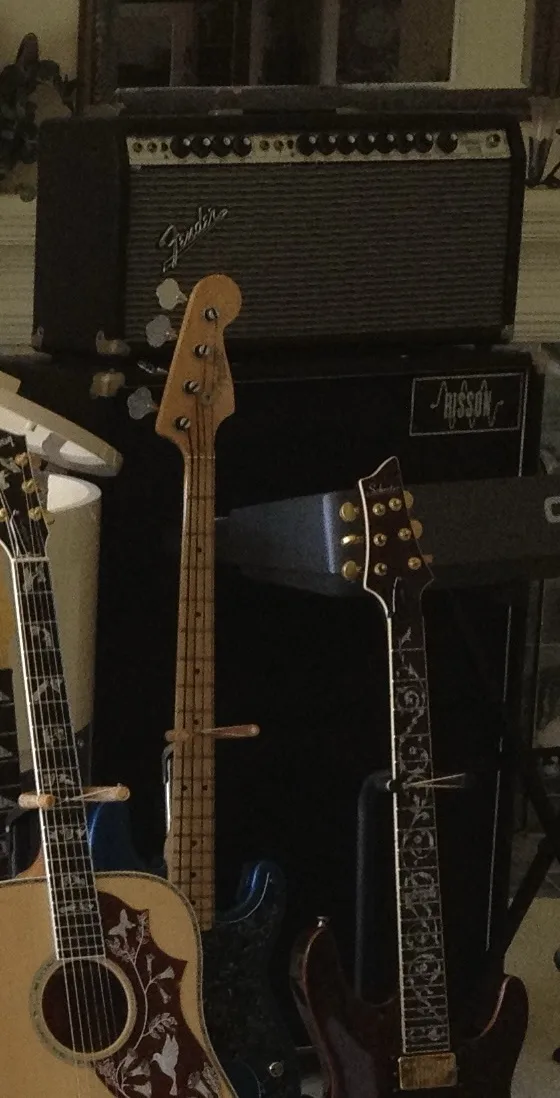 A dimly lit room shows several musical instruments including an acoustic guitar, a bass guitar, and an electric guitar…