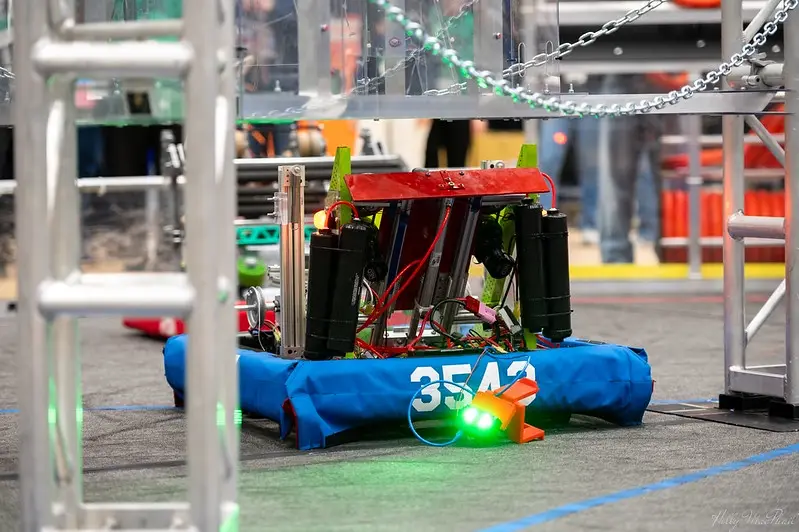 A red and black robot with visible wiring and components sits on a blue padded base marked with the number 3543. A small…