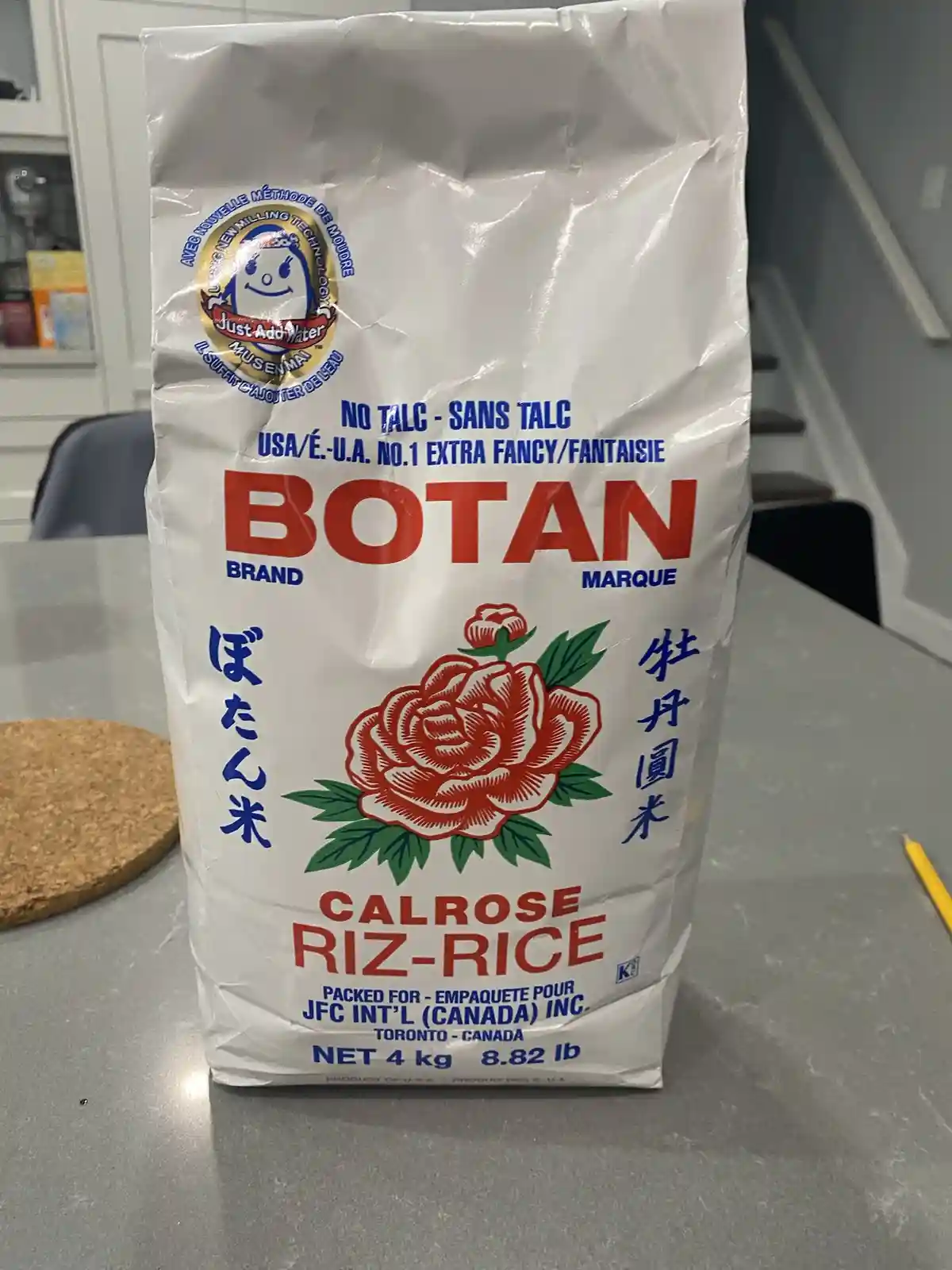 A large white bag of Botan brand Calrose rice sits on a kitchen counter, featuring a red rose logo, Japanese and Chinese…