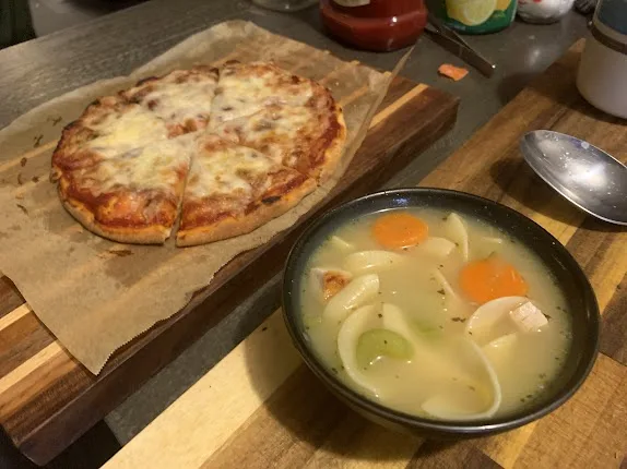 A homemade pizza with melted cheese and tomato sauce sits on parchment paper on a wooden cutting board next to a bowl of…