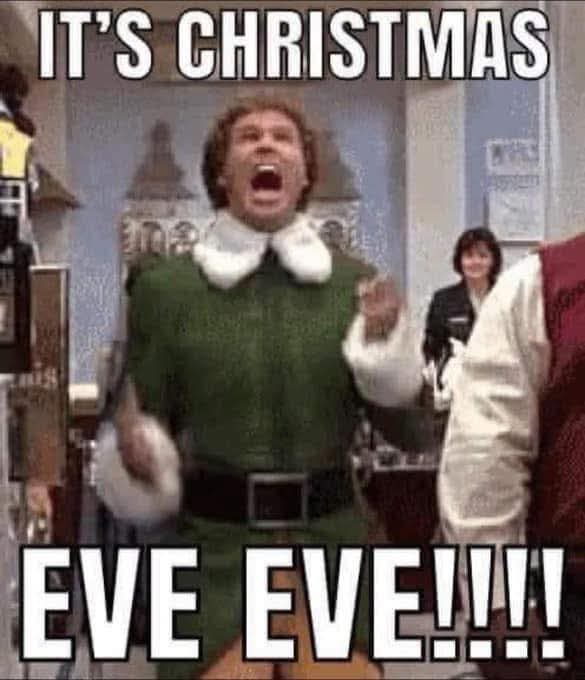 A man in a green elf costume with a white collar and black belt is shouting with his mouth wide open, arms raised in…