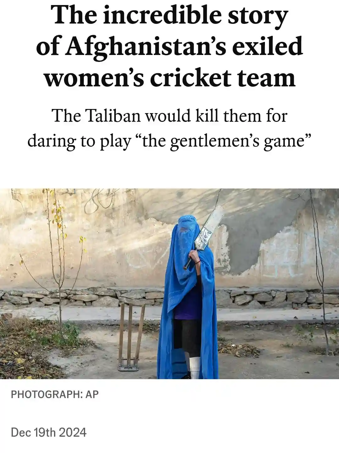 A woman wearing a blue burqa stands with her back to the camera, holding a cricket bat, next to wooden cricket stumps. The…