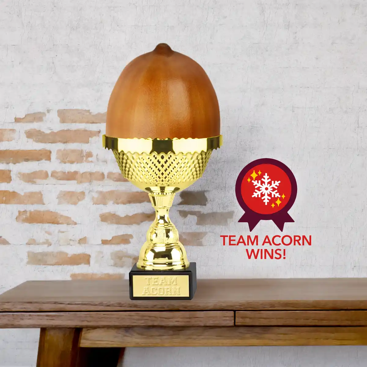 A golden trophy with a large acorn on top sits on a wooden table against a brick wall. The trophy's base is engraved with…