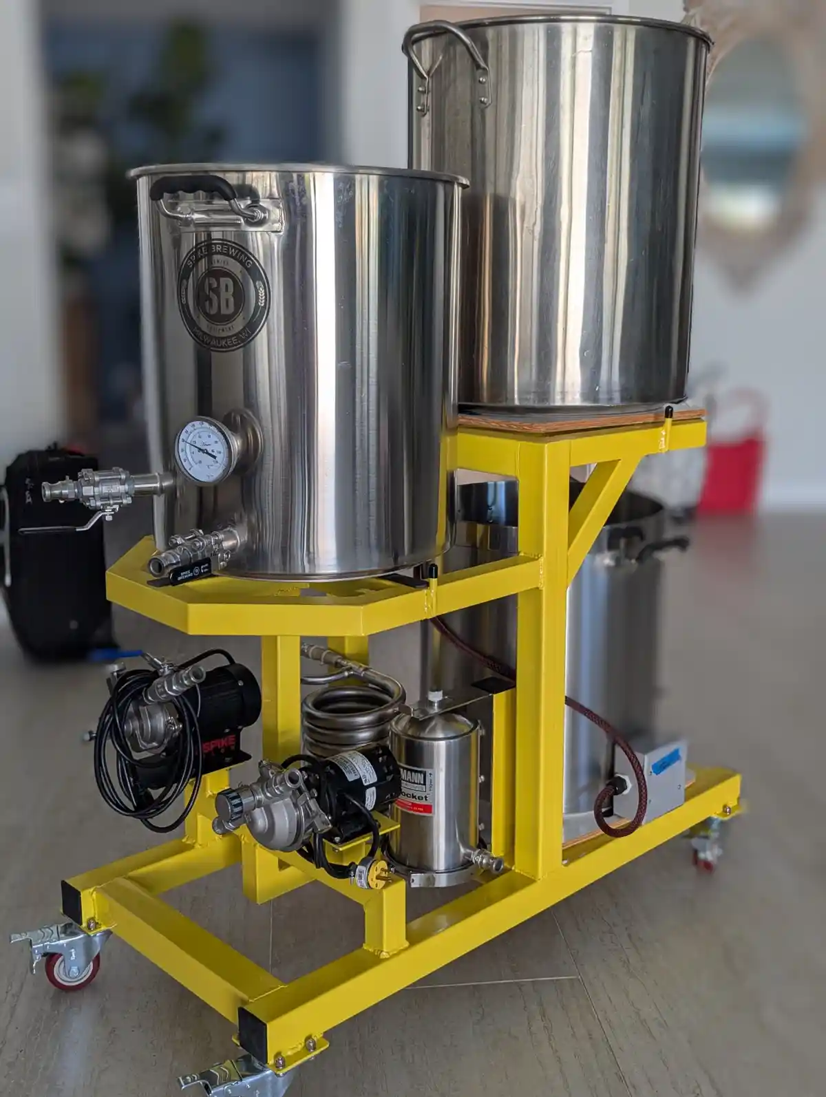 a homebrewing setup featuring two large stainless steel fermentation tanks mounted on a bright yellow metal cart with…