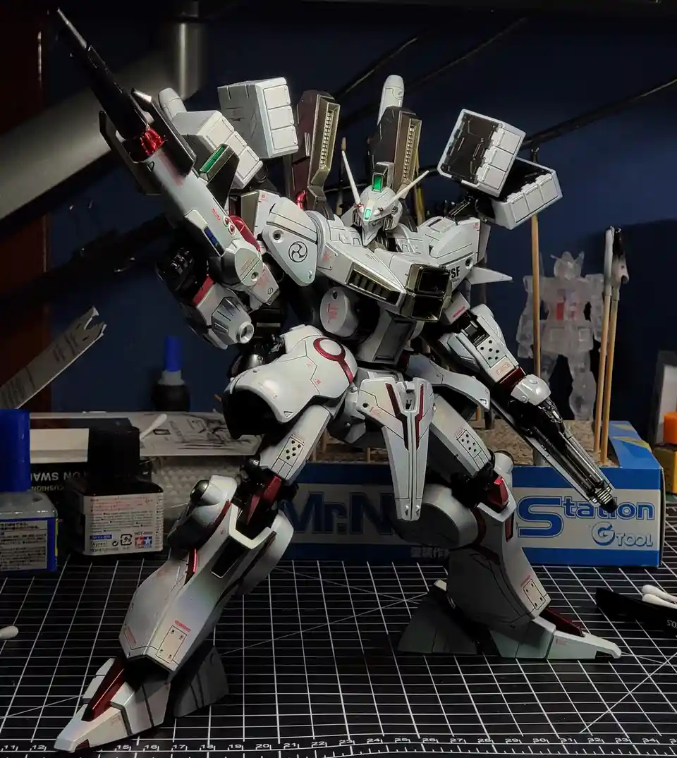 A highly detailed, white and red painted model kit of a Gundam-style robot stands on a black grid mat, holding two large…