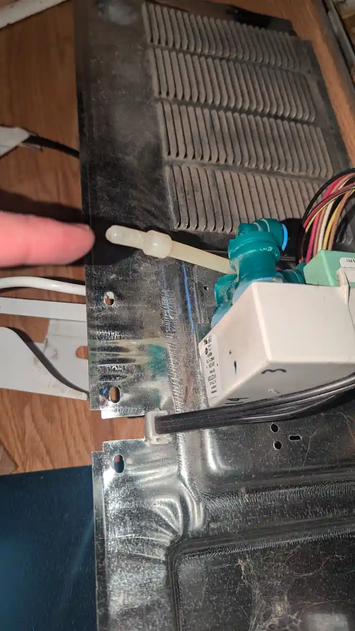 A close-up photo shows a person's finger pointing at a small, white plastic tube connected to a water valve inside a…