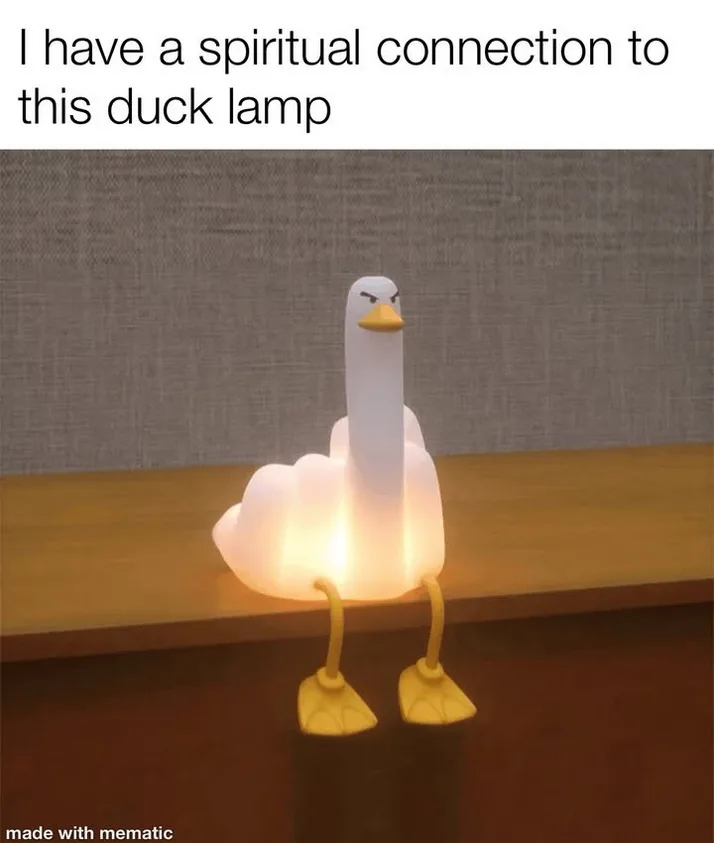 A glowing white duck-shaped lamp with an angry expression sits on a wooden surface, its yellow feet dangling below. The…