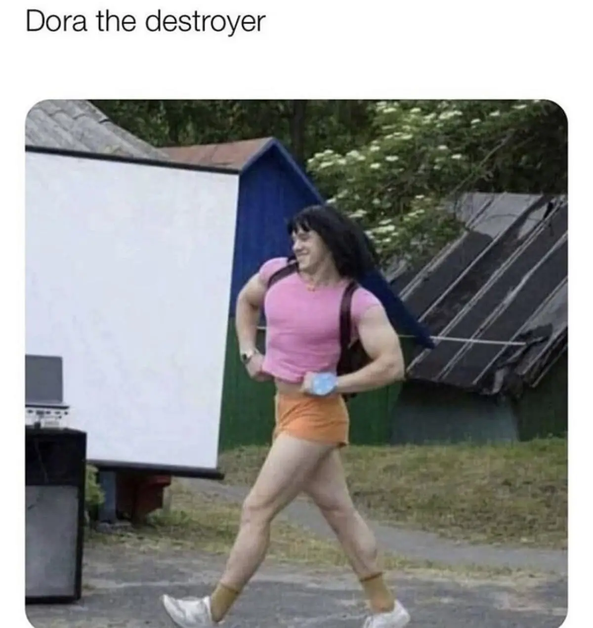 A person with a muscular build, wearing a pink crop top, orange shorts, and a backpack, walks confidently outdoors while…