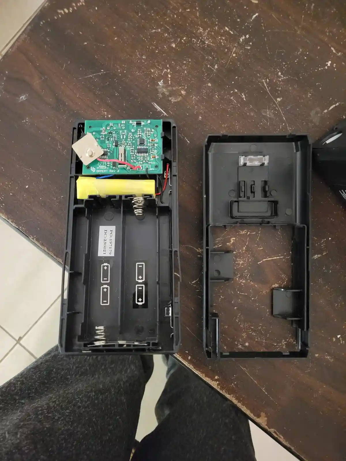 An overhead shot shows a disassembled black remote control on a scratched wooden table, with its internal green circuit…