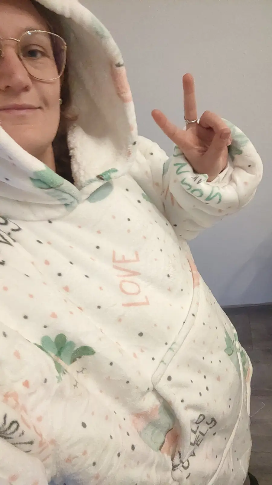 A person wearing a white, fluffy, patterned hoodie with the word 'LOVE' printed vertically in orange on the chest, makes a…