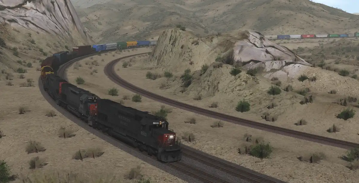 A screenshot from a train simulation game shows two trains on parallel tracks in a desert landscape. The foreground train, a…