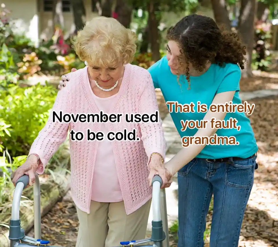 An older woman with curly blonde hair, wearing a pink cardigan and using a walker, is being supported by a younger woman in…