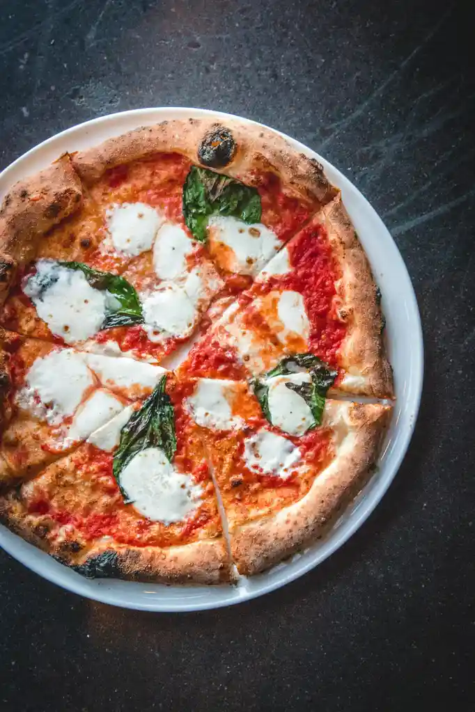 A top-down view of a freshly baked margherita pizza on a white plate, featuring tomato sauce, melted mozzarella cheese, and…