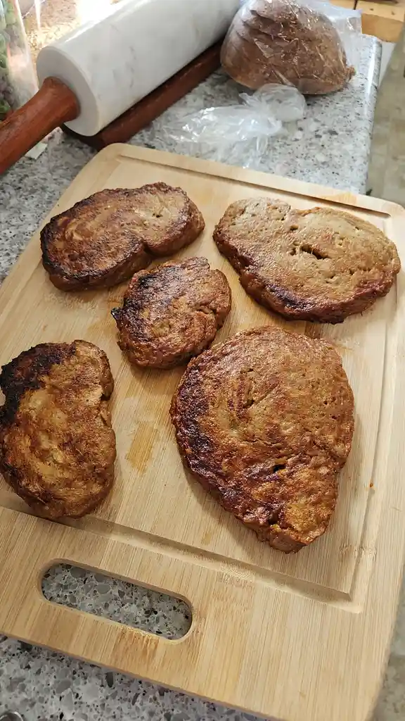 Five slices of golden-brown, slightly charred French toast sit on a wooden cutting board. In the background, a marble…
