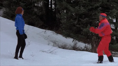 A split-screen image shows a man in a bright red and purple ski outfit performing a dramatic, exaggerated snow-shoveling…