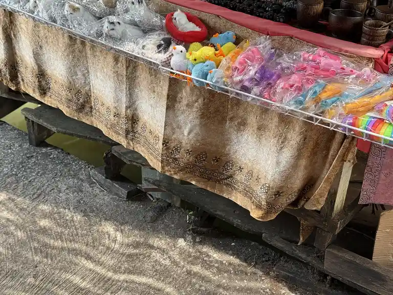 A market stall displays various plush toys, including white cat-like stuffed animals in plastic bags, colorful bird…
