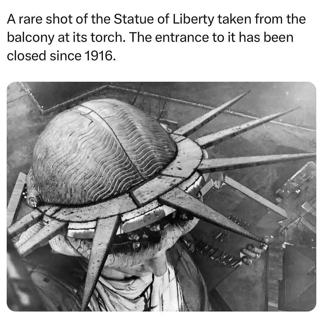A black-and-white photograph shows a high-angle view from inside the Statue of Liberty's torch, looking down at the statue's…