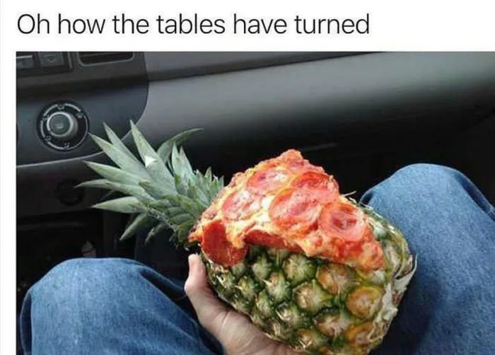 A person sitting in a car holds a pineapple with a slice of pepperoni pizza placed on top of it. The text overlay reads 'Oh…