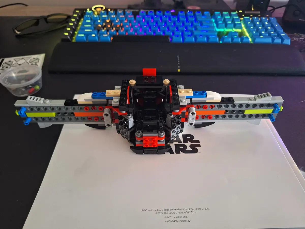 A partially assembled LEGO Star Wars X-wing fighter model sits on its instruction booklet, with a colorful backlit…