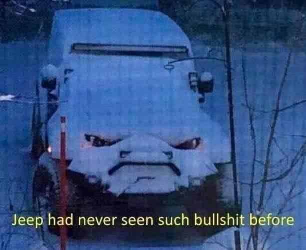 A snow-covered white Jeep appears to have an angry face, with snow forming eyebrows, eyes, and a frowning mouth. The vehicle…