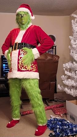 A person wearing a full-body green Grinch costume with a red Santa suit over it, standing in a living room with a white…