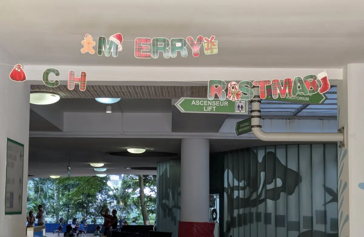 A festive indoor hallway with Christmas decorations, including plaid letters spelling 'MERRY CHRISTMAS' with gingerbread…