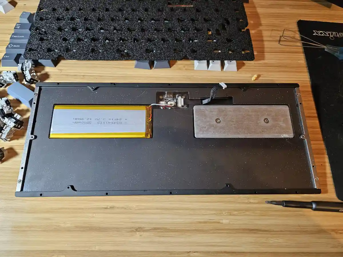 An overhead shot of a disassembled mechanical keyboard on a wooden desk, showing its internal components including a large…