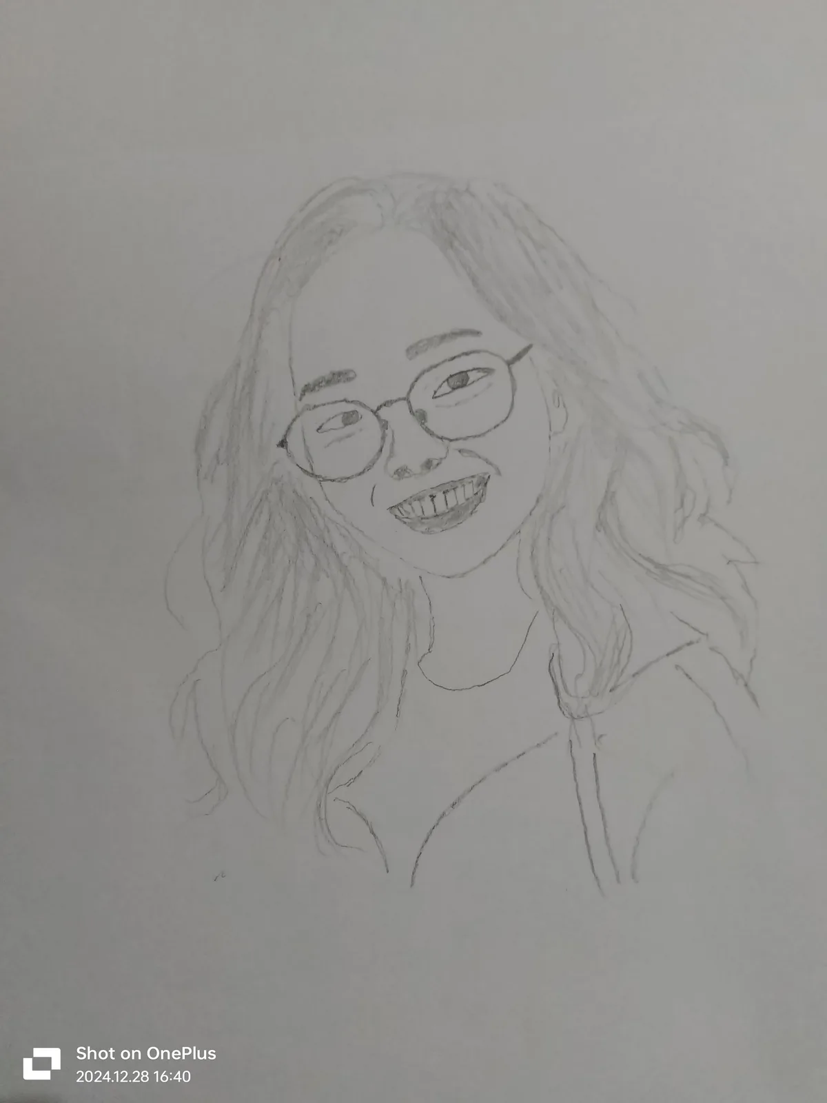 A pencil sketch of a smiling woman with glasses and wavy hair, drawn on plain paper. The image has a phone camera watermark…
