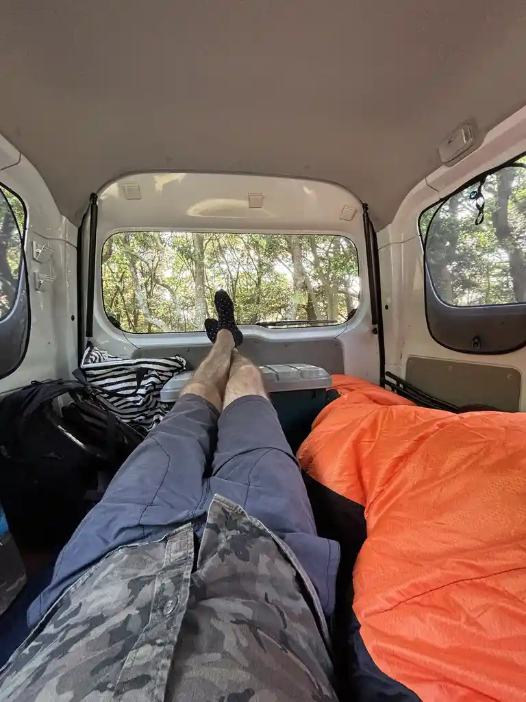A first-person view from inside a van showing a person's legs stretched out towards the rear window, wearing socks and…