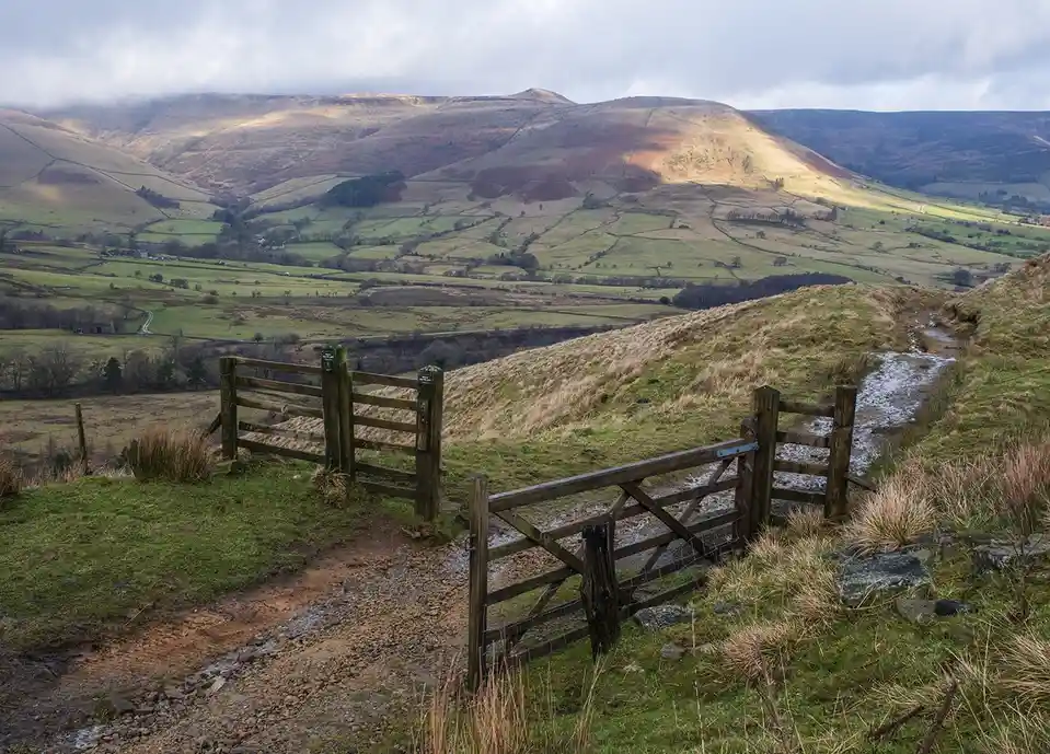a scenic rural landscape with rolling green hills, a muddy dirt path, and a wooden gate in the foreground. The overlaid text…
