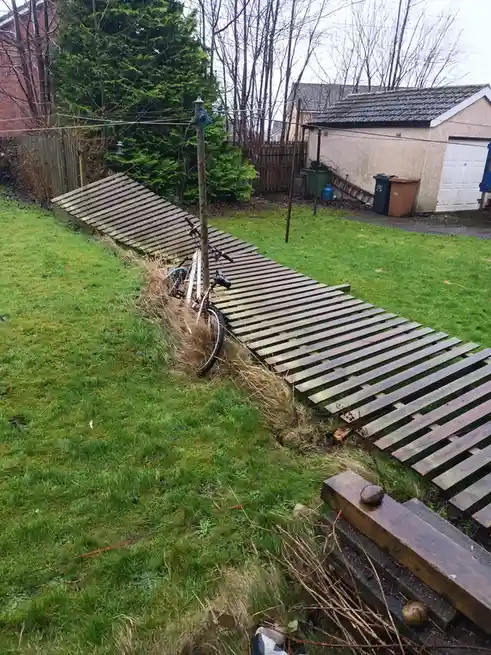 A bicycle is leaning against a wooden utility pole in a grassy backyard, with a long, sloped wooden pallet ramp extending…