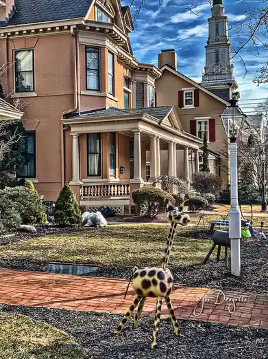 A photo of a residential street with Victorian-style houses and a church steeple under a blue sky. In the foreground, a…
