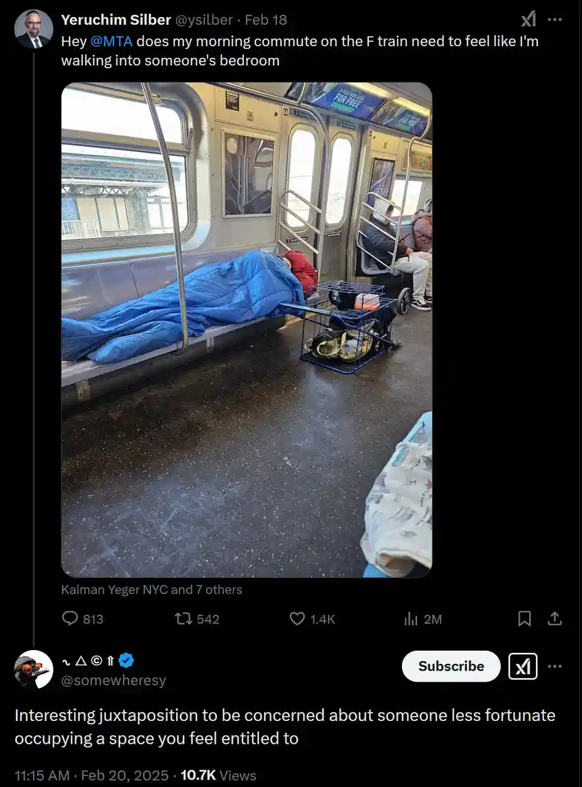 A person is sleeping on a subway train seat, fully covered by a blue sleeping bag, with a small blue cart holding personal…