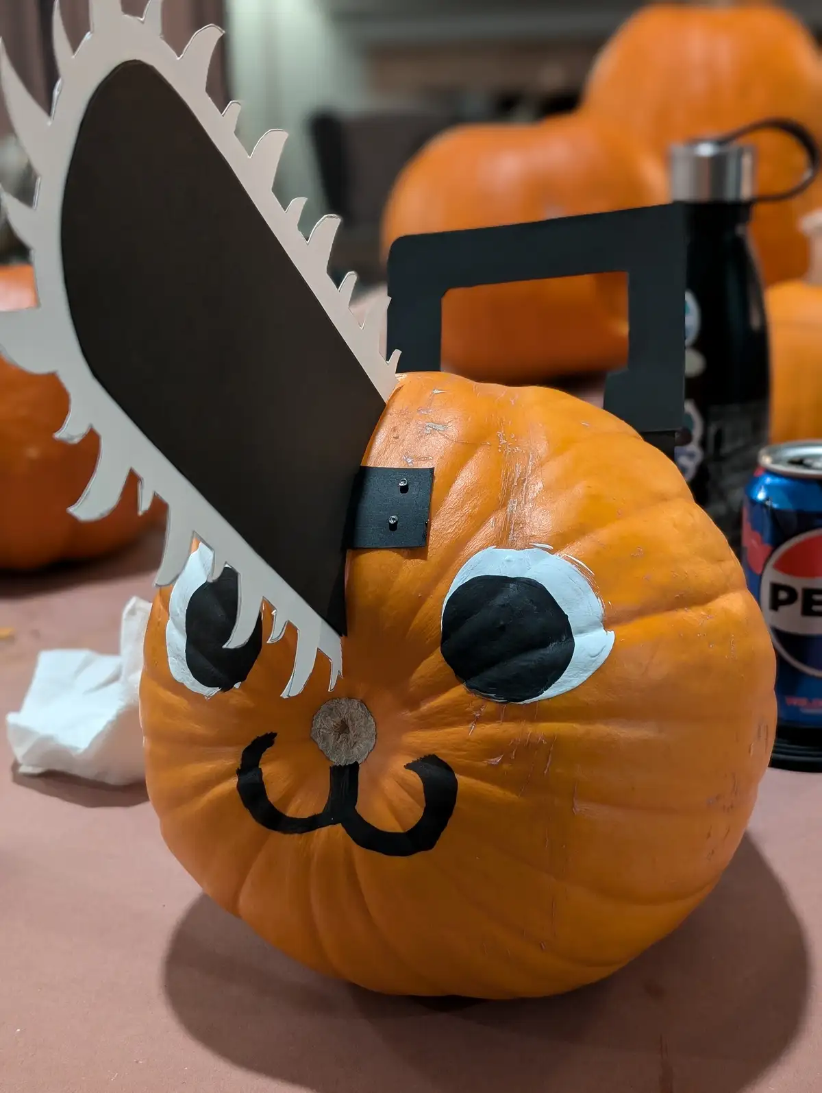 A close-up of an orange pumpkin decorated with a cartoonish face featuring large white-rimmed black eyes and a smiling…