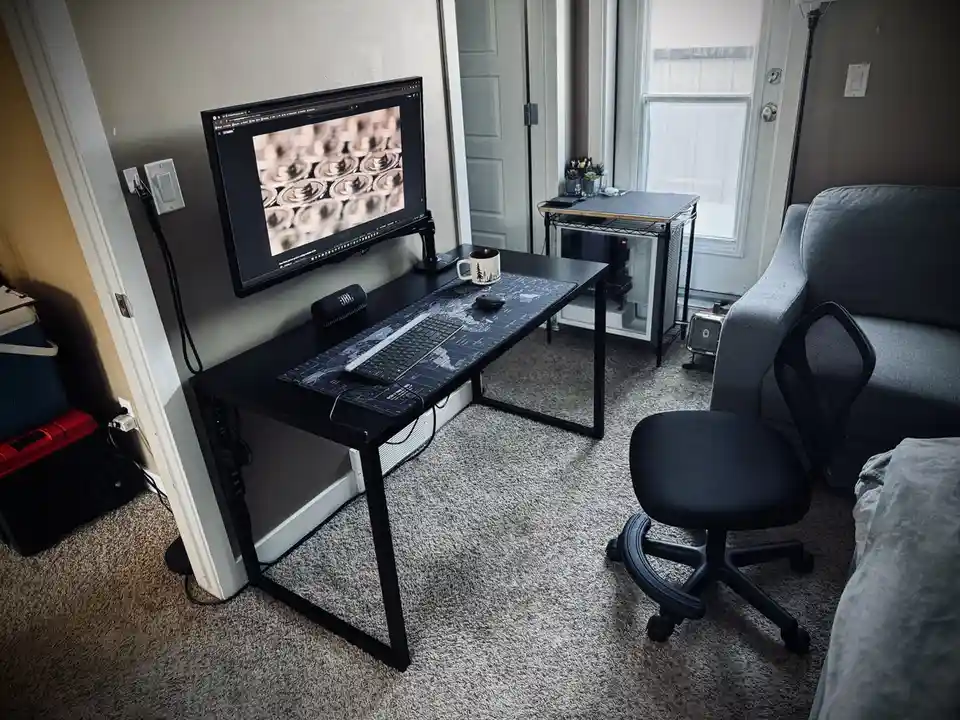 A minimalist home office setup features a black desk with a keyboard, mouse, and monitor displaying a pattern of coffee…