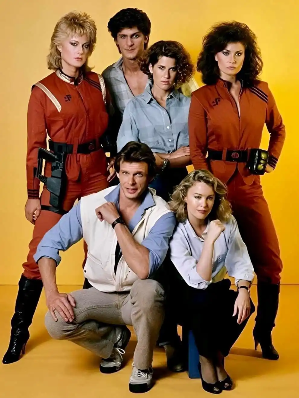 A promotional photo of the cast of the 1980s sci-fi series 'Falcon Crest' poses against a yellow background. The overlaid…