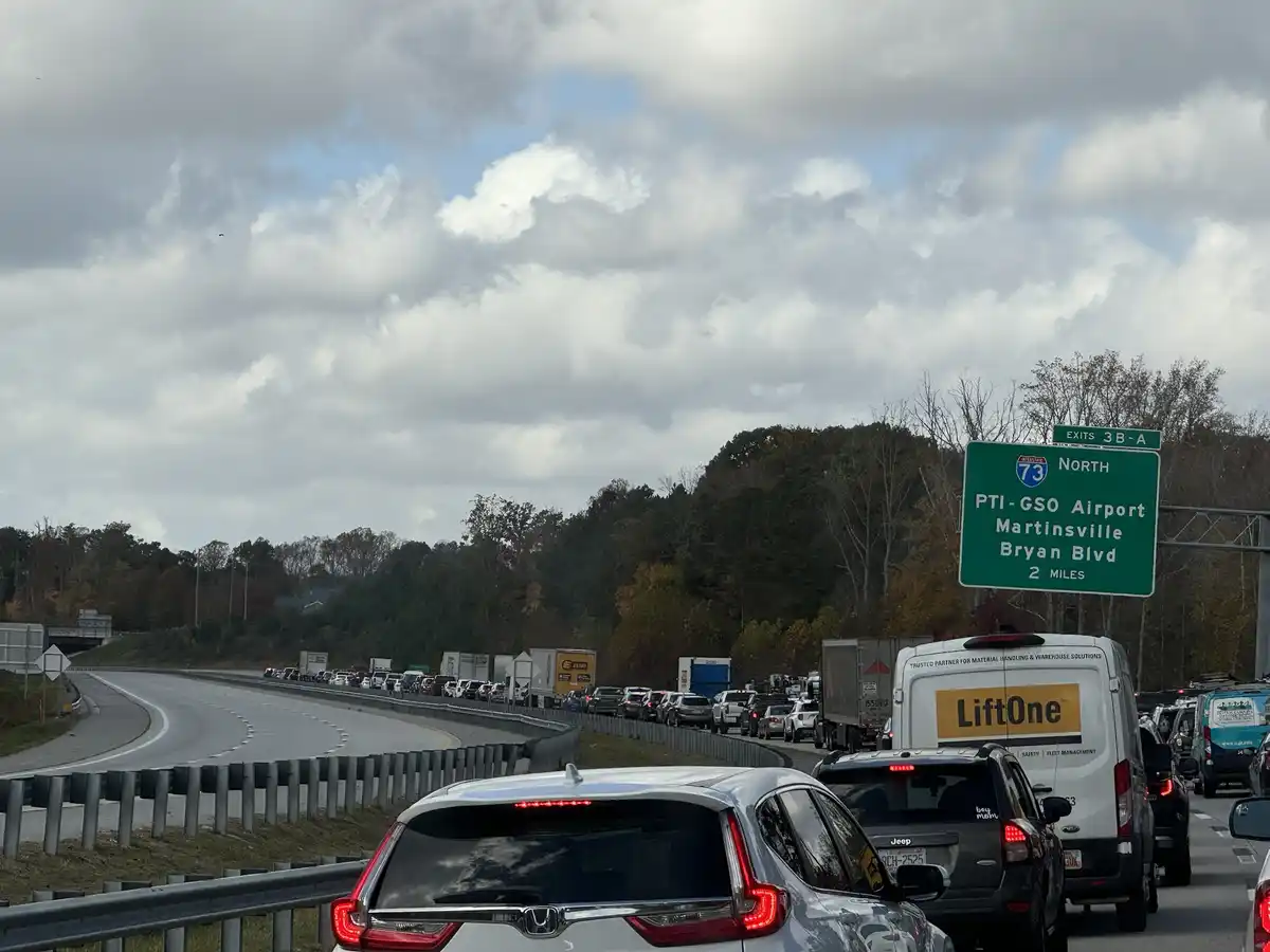 A photo of a congested highway with cars stopped in traffic under a cloudy sky. A green highway sign indicates 'I-73 NORTH'…