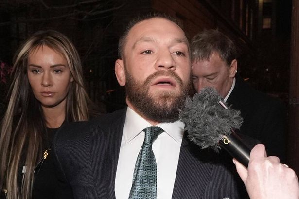 conor mcgregor, wearing a suit and tie, looks surprised or confused while being interviewed by a microphone held close to…