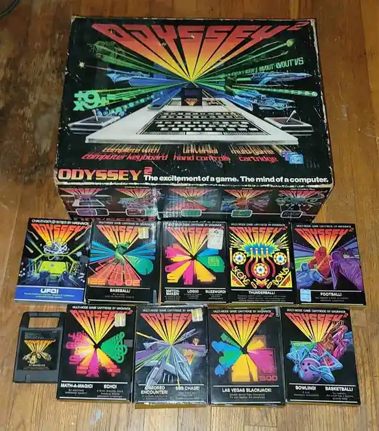 A complete Odyssey 2 video game console box sits on a wooden floor, surrounded by its original game cartridges. The box art…