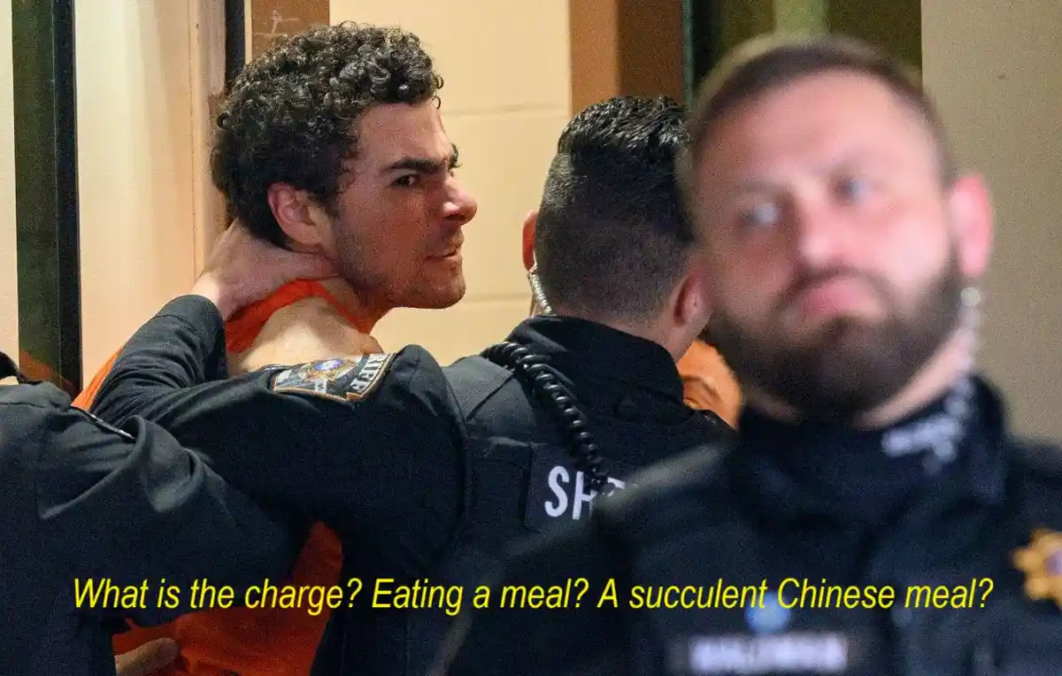 A man in an orange jumpsuit is being escorted by police officers, one holding his arm. Another officer is blurred in the…