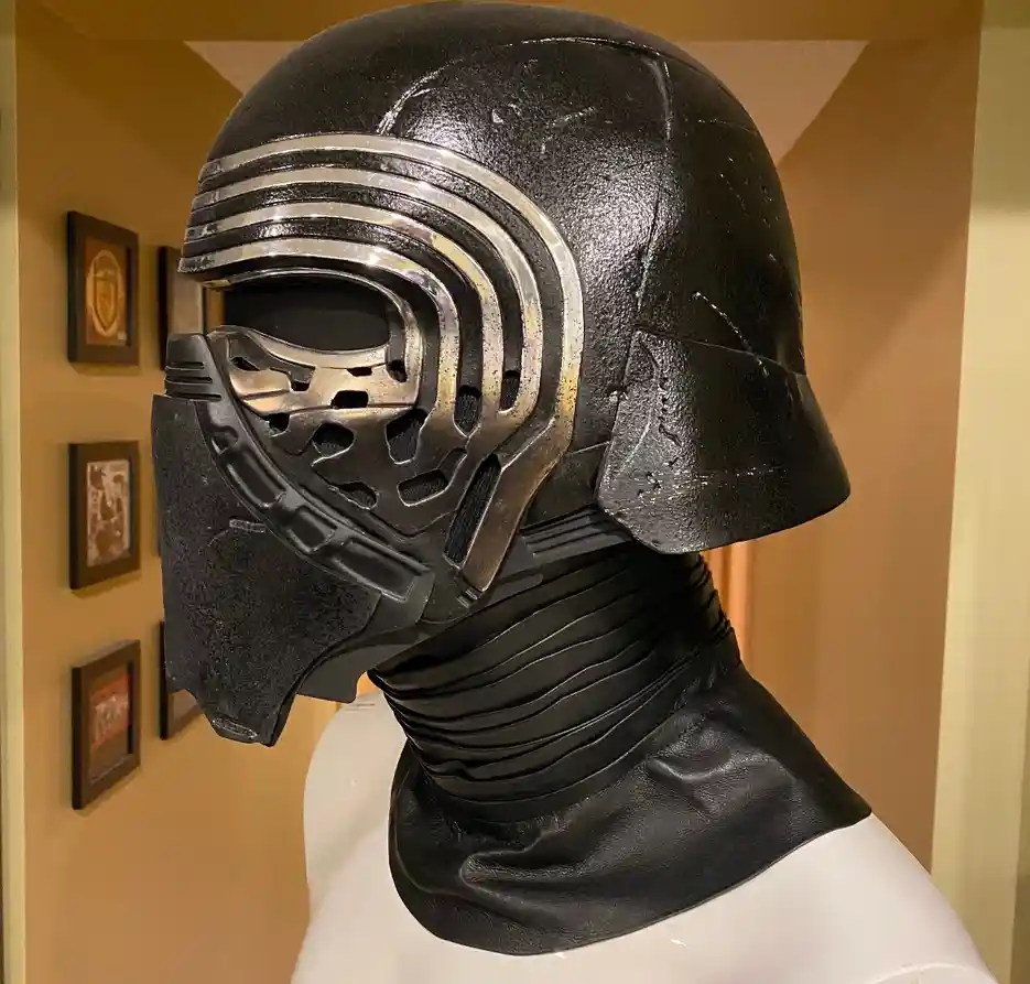 A close-up photo shows a black and silver Kylo Ren helmet from Star Wars: The Force Awakens, mounted on a white mannequin…