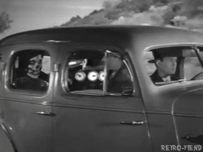A black-and-white image shows a vintage car with three men inside. The driver and front passenger are both wearing hats and…