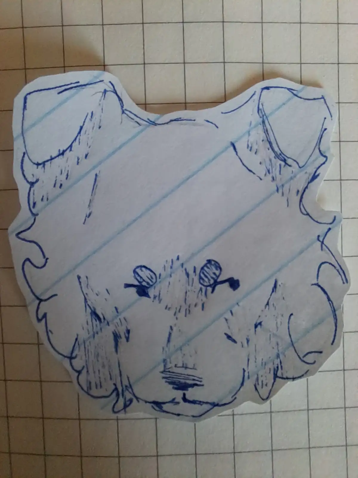 A hand-drawn, blue ink sketch on lined paper, cut into a cat's head shape, shows a cartoon cat with a sad or unimpressed…