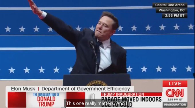 A man in a dark suit and white shirt stands at a podium with a presidential seal, raising his right arm in a gesture…